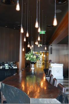 
                    
                        It’s big, bold and heavy. And it’s the first thing, apart from the maitre d’ that greets you upon entering.  This signature restaurant comes with a signature piece of furniture ~ a ginormous $12,000 dining table made out of a single tree.  Interior designer Paul Kelly’s team found the tree in Oberon near the Blue Mountains in country New South Wales. It was sliced in half and its jagged edges sanded down.
                    
                